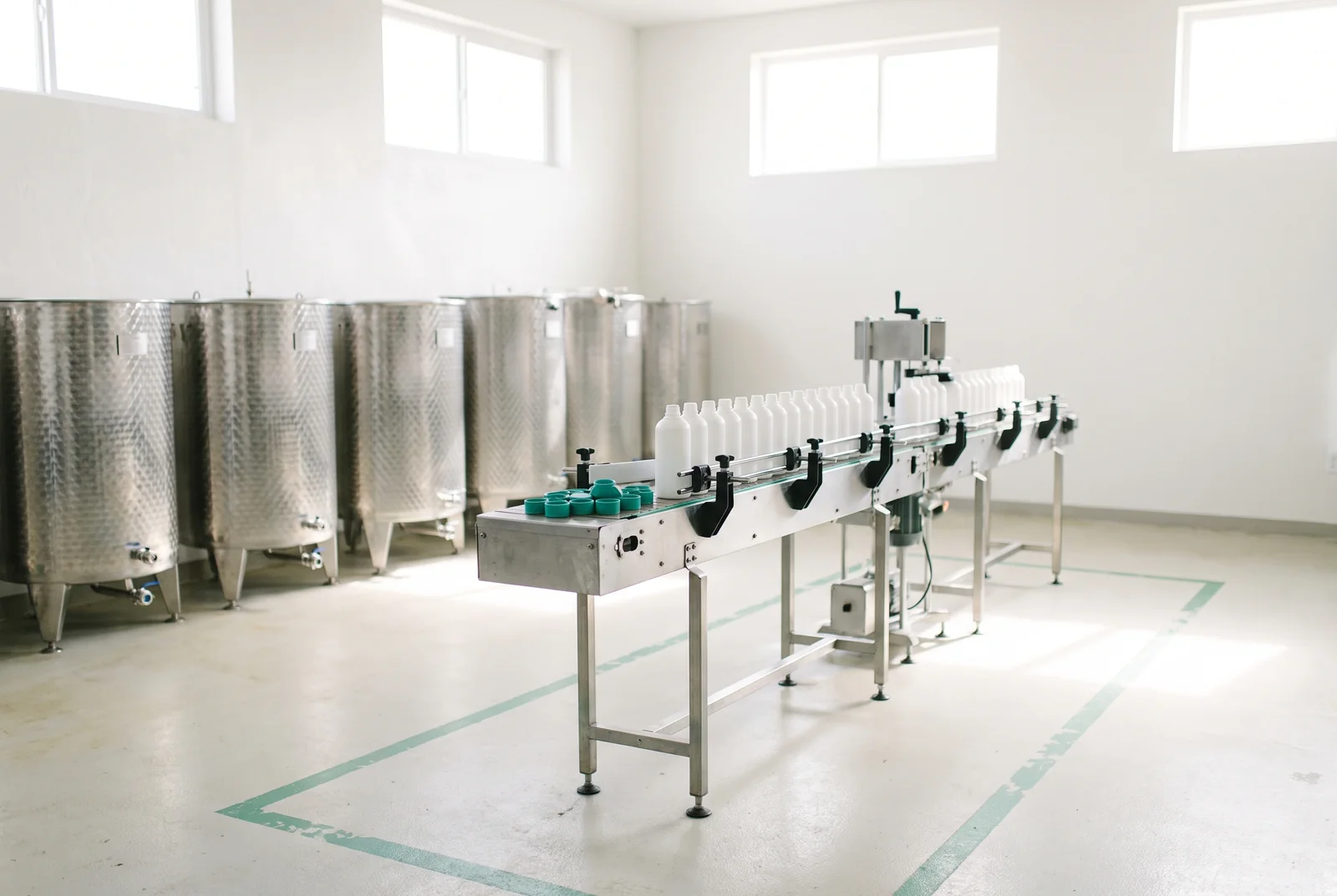 Planta de envasado de productos de limpieza, con tanques de acero y una línea de llenado.